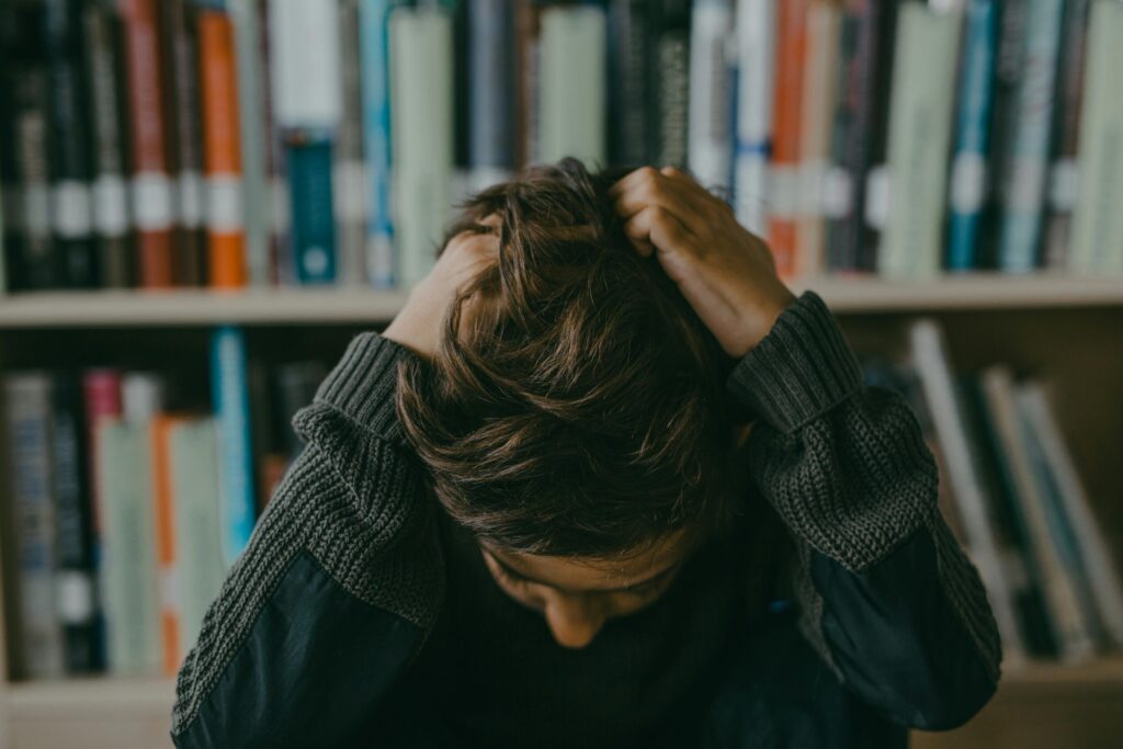 A child appears stressed and frustrated while seated in a library, holding their head.